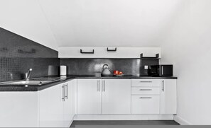 Una cucina moderna con un piano di lavoro nero, mobili bianchi, un bollitore e un forno a microonde.