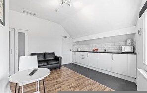 Una cucina moderna con mobili bianchi, un divano in pelle nera, un tavolo bianco e un telecomando sul tavolo.