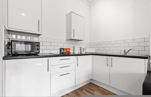 A modern kitchen with white cabinets, a microwave, and a sink. - Large Modern Leeds Stay w 8 Private Ensuite Studio (Leeds)