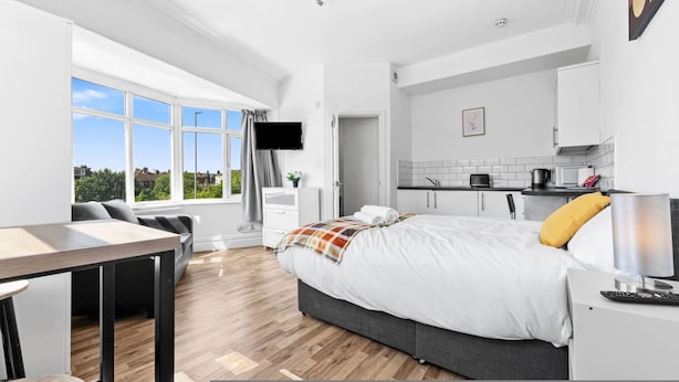 A modern hotel room with a large bed, a dining area, a kitchenette, and a TV mounted on the wall. - Large Modern Leeds Stay w 8 Private Ensuite Studio (Leeds)