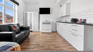 A modern kitchen with white cabinetry, a flat-screen TV, and a black leather sofa. - Large Modern Leeds Stay w 8 Private Ensuite Studio (Leeds)