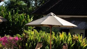 A poolside area with lounge chairs, a covered umbrella, and a thatched-roof structure. - Co Day Uluwatu  (Pecatu)