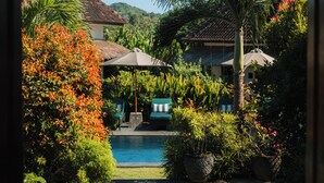 A tropical garden with a pool, palm trees, and a thatched-roof building. - Co Day Uluwatu  (Pecatu)