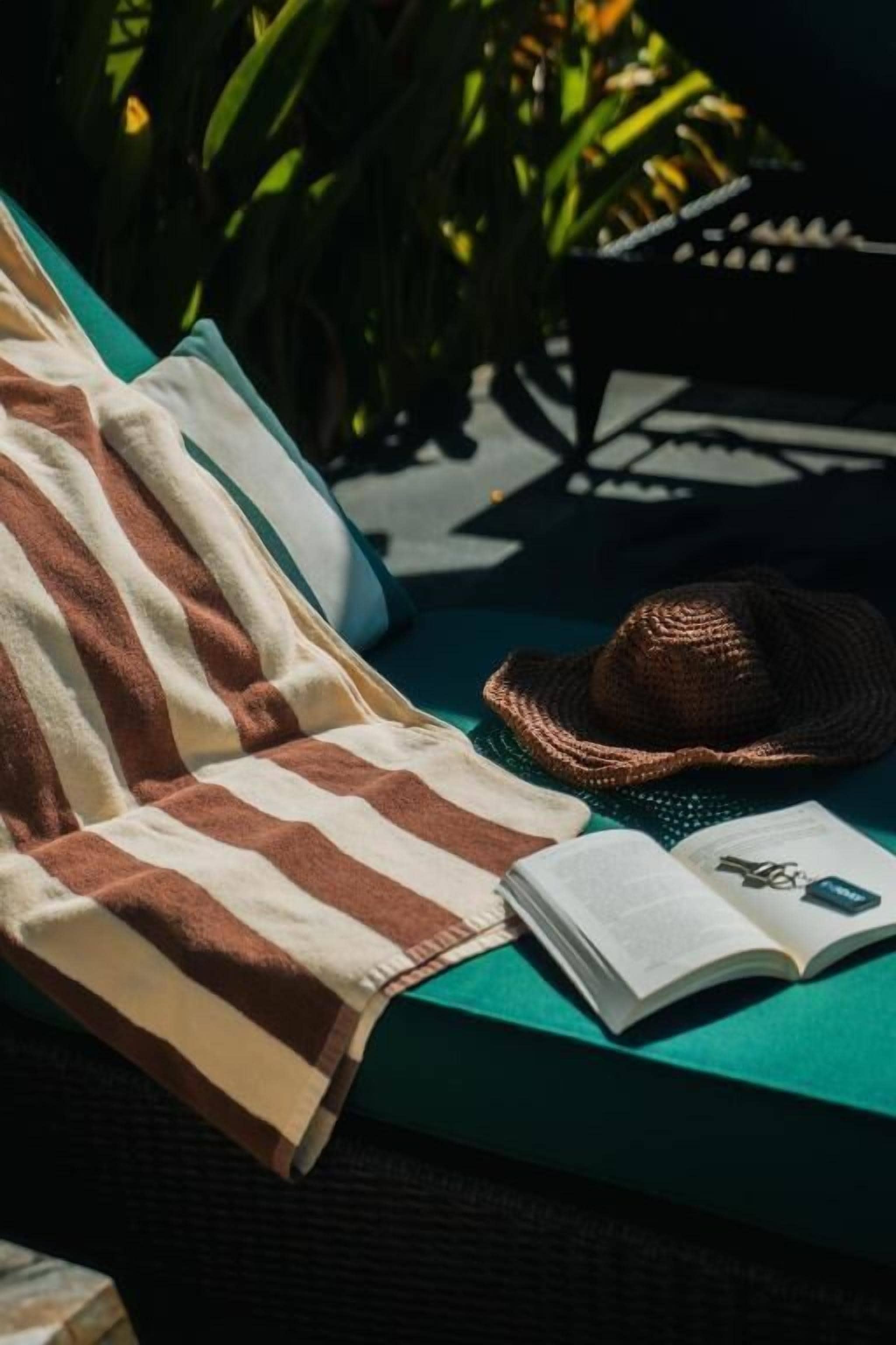 A lounge chair with a striped towel, a hat, and an open book.