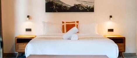 A bedroom with a bed, a bench, two bedside tables, a wall-mounted air conditioner, and a painting.