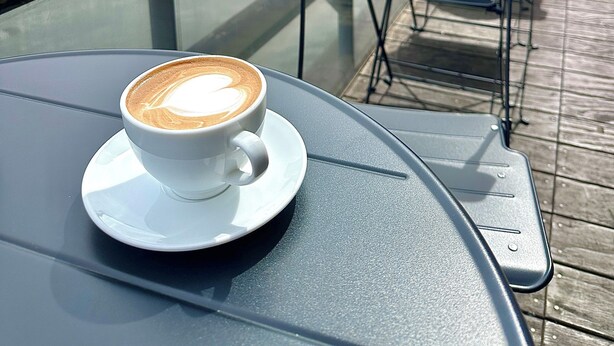 Une table avec une tasse de café, une chaise et une vue sur une rivière, avec des bâtiments en arrière-plan.
