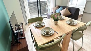 Un coin repas avec une table dressée pour deux personnes, un canapé et une vue sur l’extérieur.