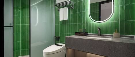 A modern bathroom with green tiles, a toilet, a shower enclosure, and a vanity with a mirror.