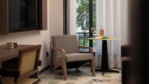 A modern room with a flat-screen TV, a dining table, a chair, a small table with a glass of wine, and a view of trees outside. - K.K Fashion Hotel (Chongqing)