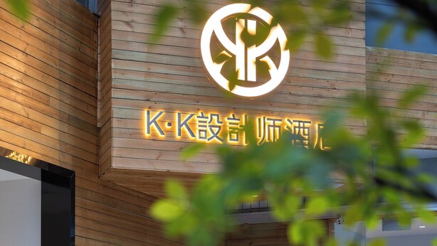 A wooden wall with a logo and text, a table with chairs, and a glass door. - K.K Fashion Hotel (Chongqing)
