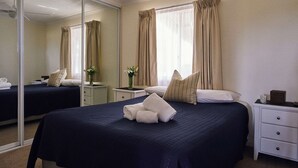 A hotel room with a large bed, a bedside table, a mirror, and a window with curtains. - Meroo Hous - Three-Bedroom Home with Sea Views (Mollymook)