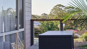 A balcony with a wicker chair, a glass door, and a view of trees and buildings. - Meroo Hous - Three-Bedroom Home with Sea Views (Mollymook)