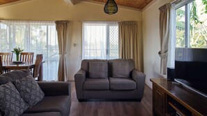 A living room with a sofa, a TV, and a dining area with a table and chairs. - Meroo Hous - Three-Bedroom Home with Sea Views (Mollymook)
