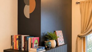 En öppen spis med en svart mantel, ett stort, abstrakt konstverk och en samling böcker och dekorativa föremål.