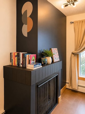 A fireplace with a black mantel, a large abstract number, and a collection of books and decorative items. - Charming 2Bd Apartment in Downtown Calgary (Calgary)