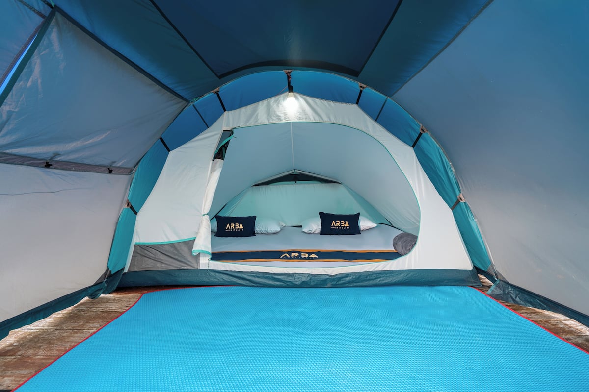 Tienda de campaña con zona de descanso, que incluye una cama y almohadas con la marca 'ARBA'.
