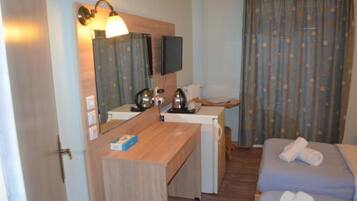 Ett hotellrum med ett skrivbord i trä, en tv, en säng och en duschhörna.