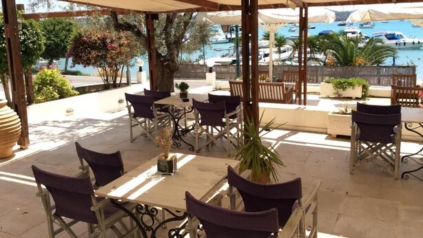 Un patio al aire libre con mesas y sillas, una pérgola y vistas a barcos en el agua.