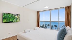 A bedroom with a large window, a flat-screen TV, and a bed with pillows.