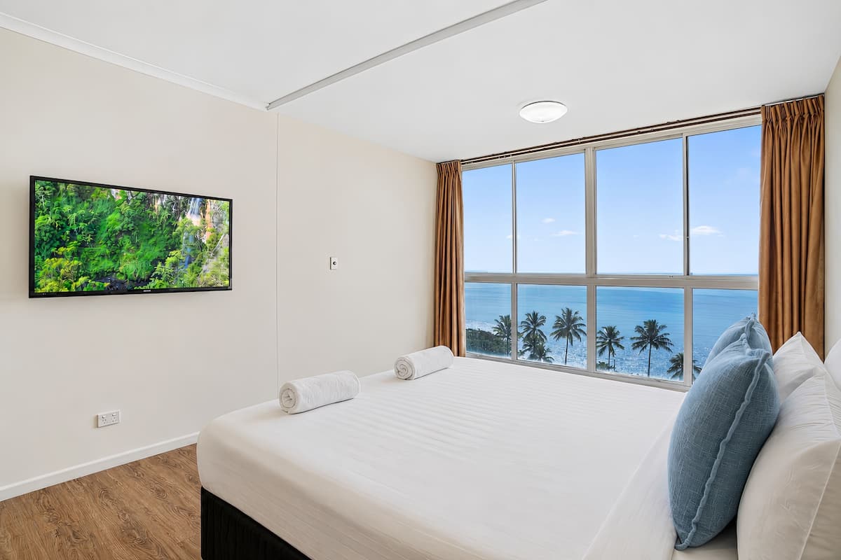 Un dormitorio con un ventanal grande, un televisor de pantalla plana y una cama con almohadas.