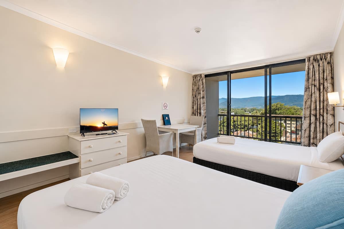 A hotel room with a bed, a desk, a chair, a TV, and a balcony with a view.