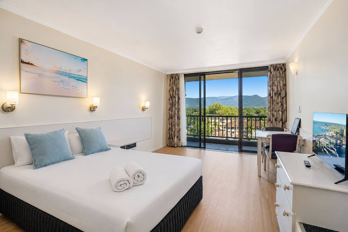 Habitación de hotel con cama, escritorio, televisión y balcón con vistas.
