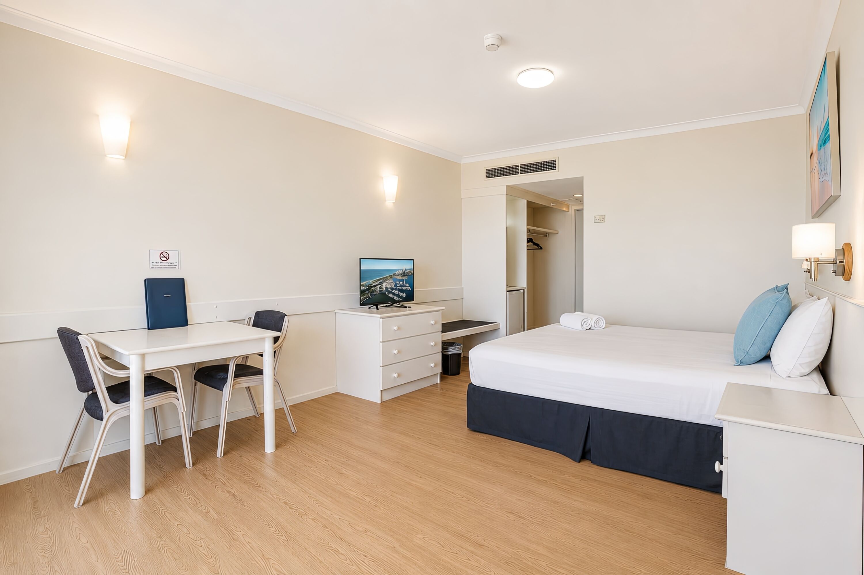 A room with a bed, desk, chair, and a painting on the wall.