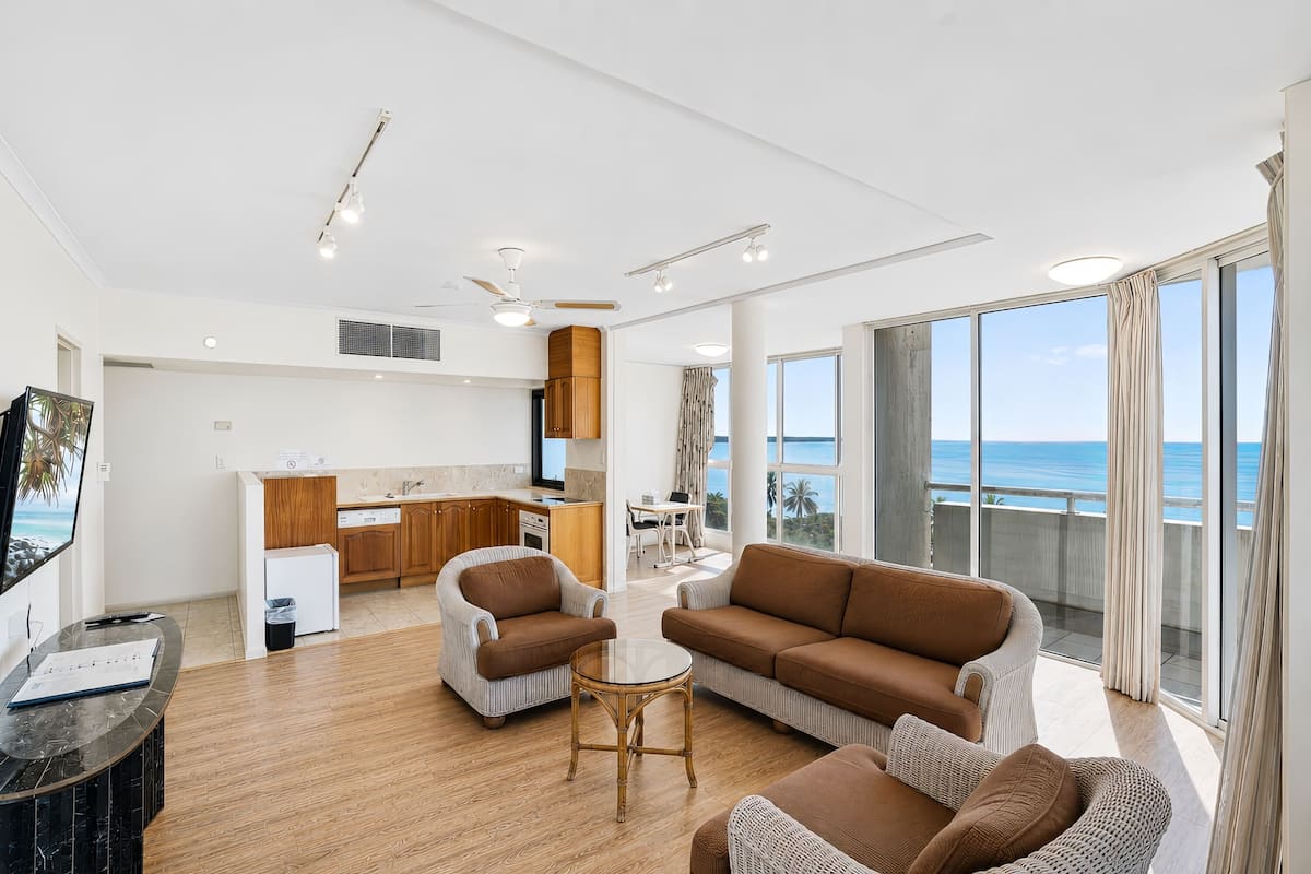 Amplia sala de estar con un ventanal grande, cocina y balcón con vista al mar.