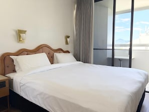 A hotel room with a large bed, two bedside tables, a small table by the window, and a view of the cityscape. - The Oceanfront Cairns (Cairns)