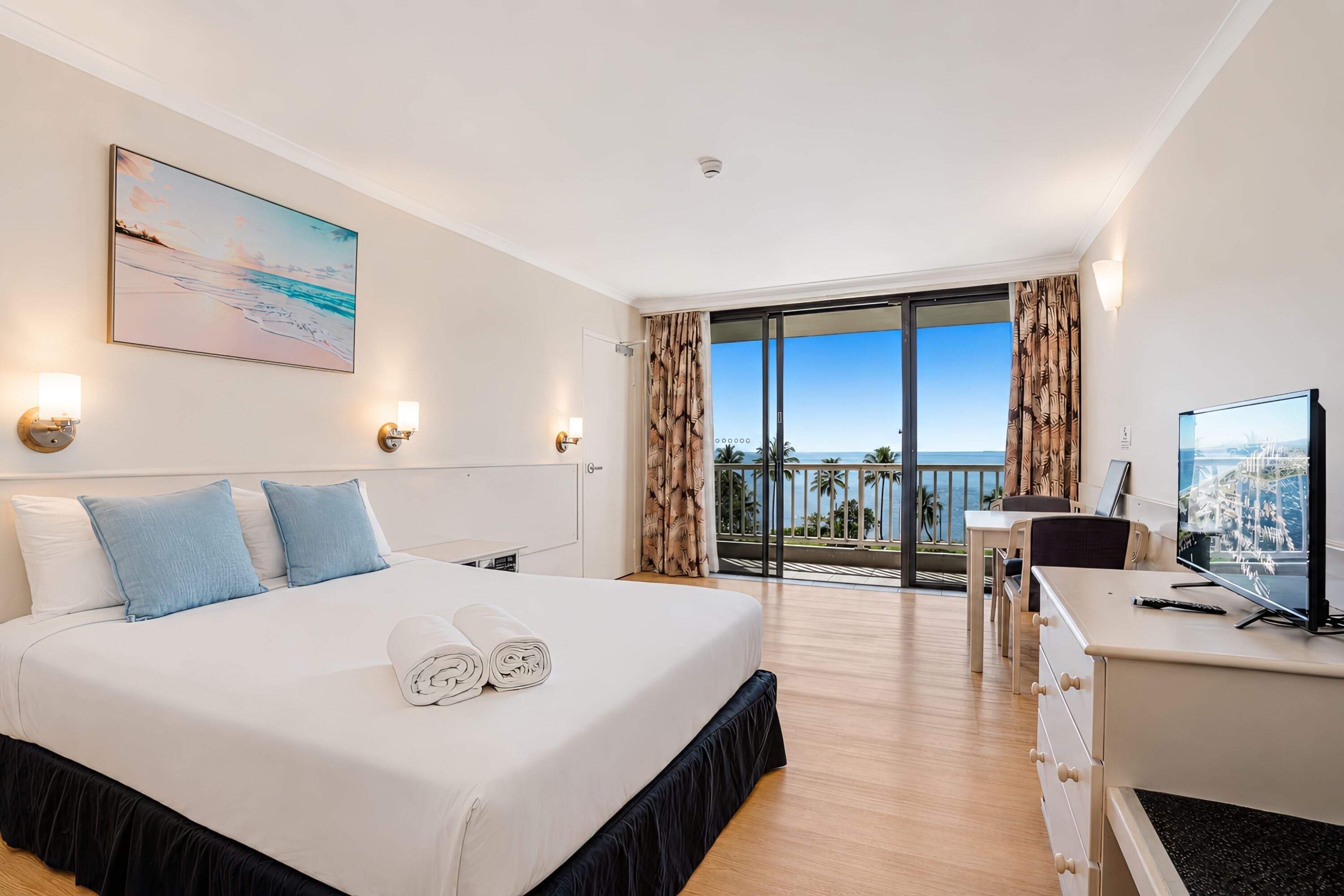 A hotel room with a bed, a desk, a TV, and a balcony with a view.