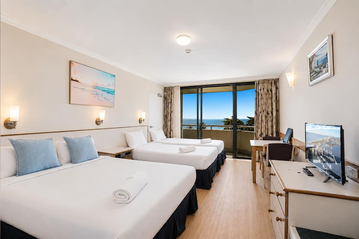 Habitación de hotel con dos camas, un escritorio, un televisor y un balcón con vistas.
