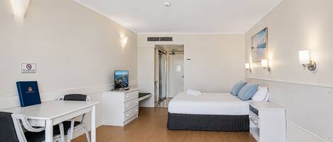 Une chambre d’hôtel comprenant un lit, un bureau, une chaise, une commode et une porte donnant sur une autre pièce.