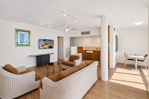 Una sala de estar moderna con un conjunto de sofás, una mesa de comedor y una zona de cocina con armarios de madera.