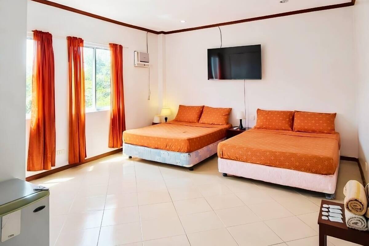 Habitación de hotel con dos camas, televisor, escritorio y ventana con cortinas.