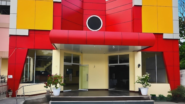 Un edificio moderno con fachada roja y amarilla, ventanas amplias y un ventanal circular sobre la entrada.