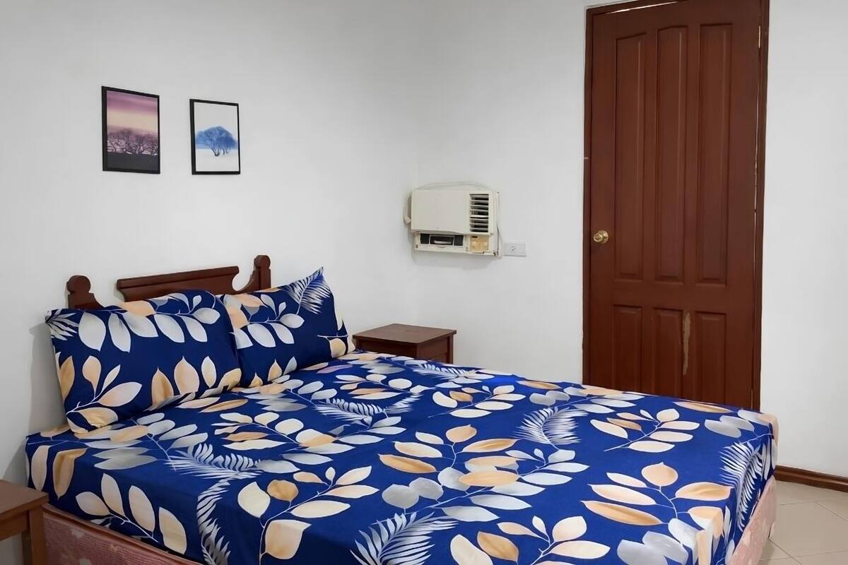 Un dormitorio con cama, mesita de noche, equipo de aire acondicionado y una puerta.