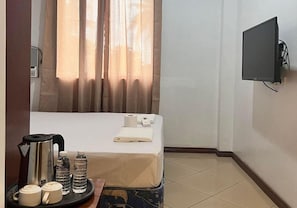 Une chambre dâhĂŽtel avec un lit, un tĂ©lĂ©viseur fixĂ© au mur, un plateau avec une bouilloire, des bouteilles dâeau et des tasses.