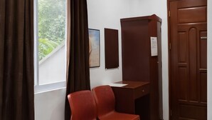 Una habitación con escritorio, dos sillas, ventana con cortinas, puerta y un tablón de anuncios en la pared.