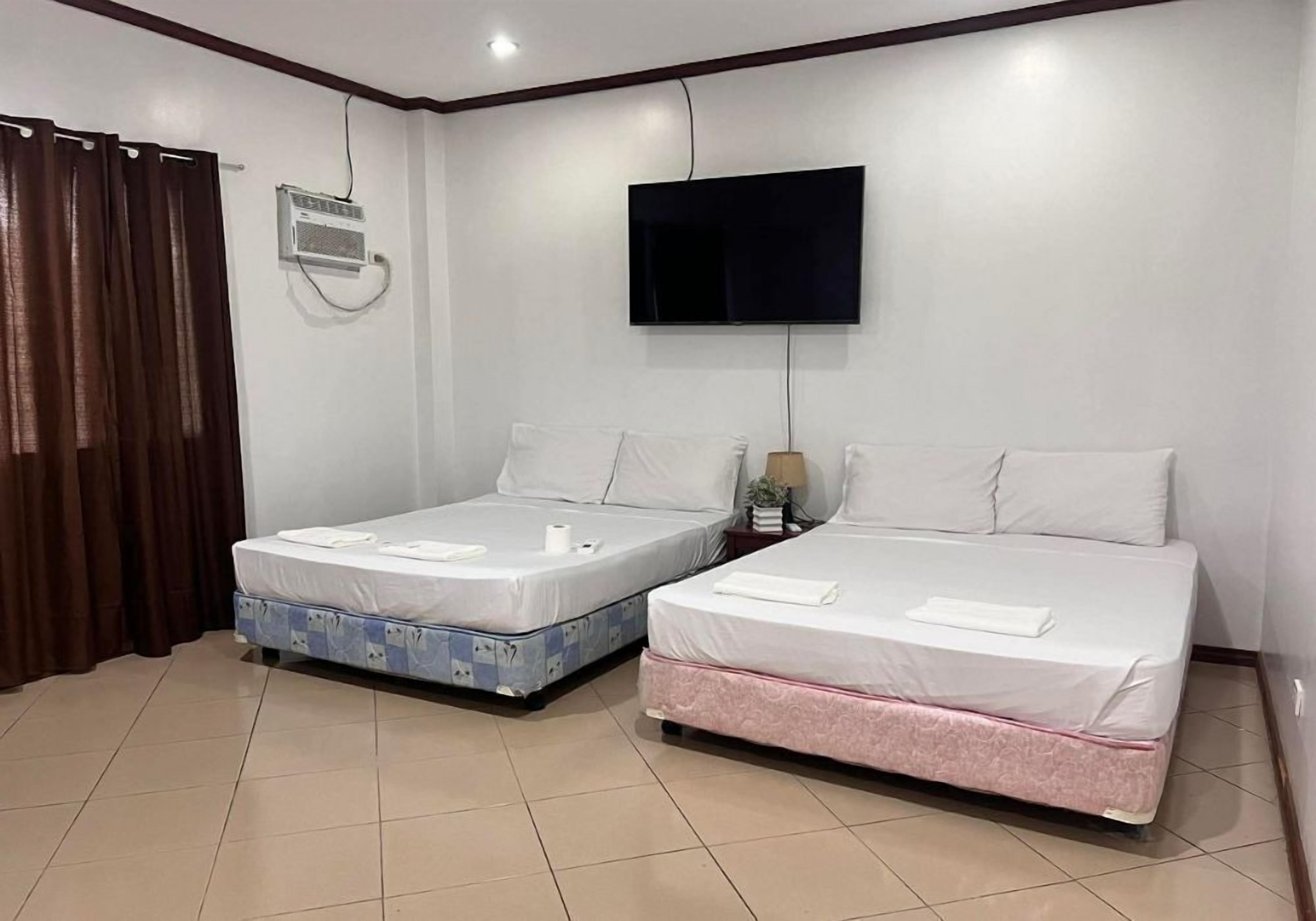 A hotel room with two beds, a TV, an air conditioning unit, and a curtain.