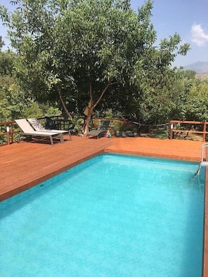 Ein klares, blaues Schwimmbecken mit Holzterrasse und Liegestühlen.