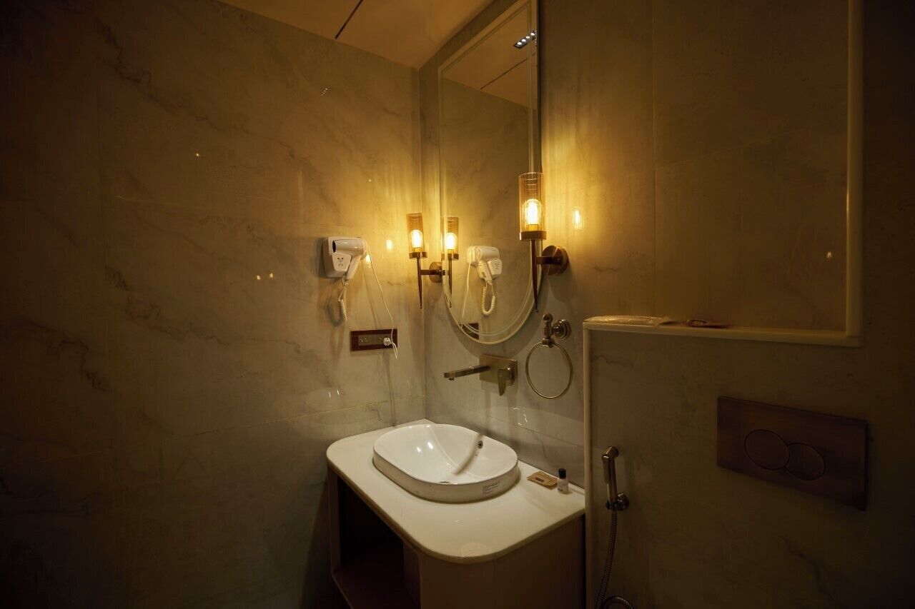 A bathroom with a marble wall, a sink, a mirror, and two wall-mounted hair dryers.