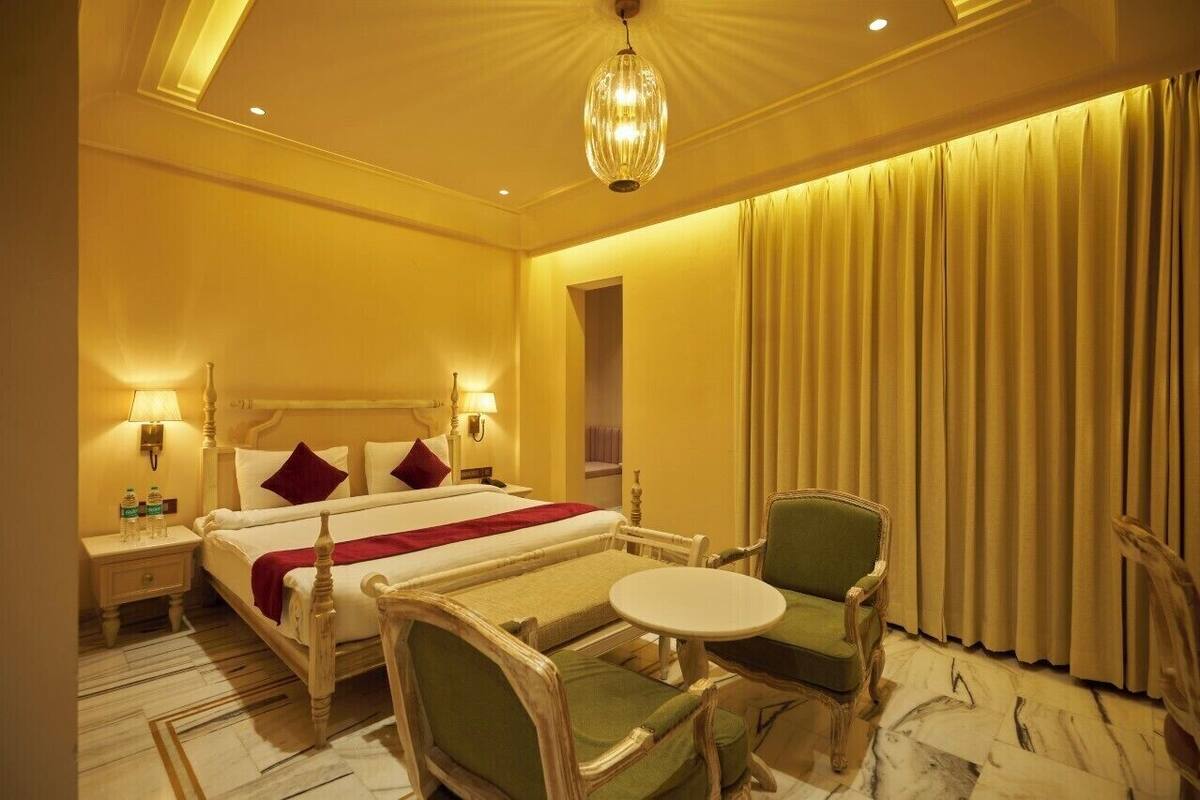 Habitación de hotel con cama, mesitas de noche, lámpara, silla, una pequeña mesa y cortina.
