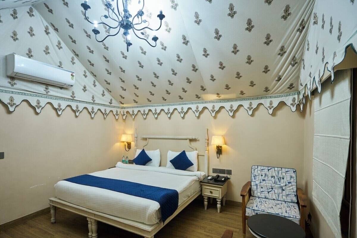 Un dormitorio con cama, lámparas de noche, una silla, una mesita y un equipo de aire acondicionado.