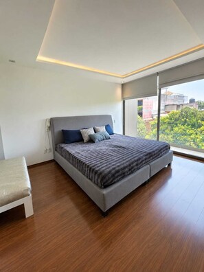 A modern bedroom with a large bed, a bench, and a view of greenery through large windows. - Modern, luxurious and centrally located minimalist house near the WTC (Del Valle Nte)