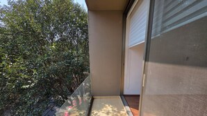 Ein Balkon mit Glastür, Fliesenboden und Blick auf dichtes Grün.
