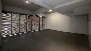 Ein geräumiger Raum mit hoher Decke, eingelassener Beleuchtung und einem großen Fenster mit horizontalen Jalousien.
