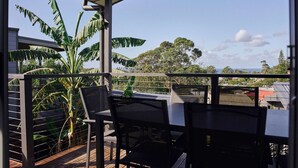 Een balkon met een tafel en stoelen, een bloempot en uitzicht op bomen en gebouwen.