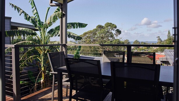 Un balcon avec une table et des chaises, un pot de fleurs et une vue sur les arbres et les bâtiments.
