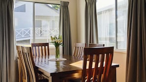 Une table à manger avec des chaises, un vase de fleurs et des rideaux aux fenêtres.