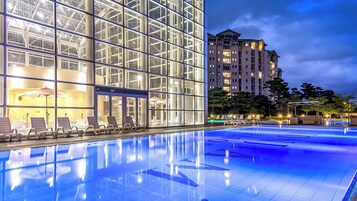 Una piscina con sillones de descanso, un edificio de vidrio con diseño moderno y un rascacielos al fondo.